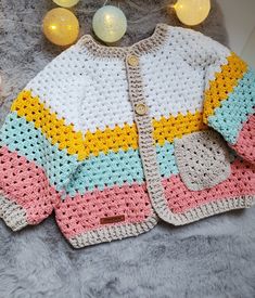 a crocheted sweater is laying on a furry surface next to some christmas lights