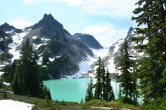 the mountains are covered in snow and green pine trees, with a lake below them