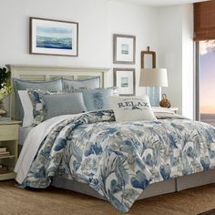 a bed with blue and white comforter in a bedroom next to a window overlooking the ocean