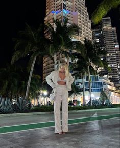 a woman standing in front of tall buildings at night with her hands on her hips