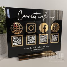 a black and gold sign with qr code on it next to a potted plant