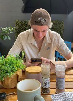 a woman sitting at a table looking at her cell phone and holding a coffee cup