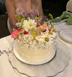 a woman sitting at a table in front of a white cake with flowers on it