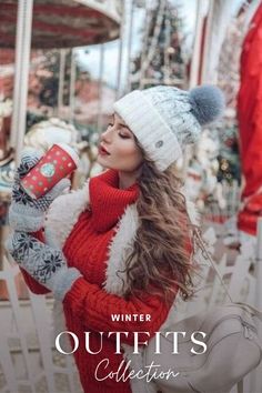 a woman in a red sweater and white hat holding a coffee cup while standing next to a carousel