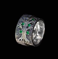 a silver ring with green stones in the middle and a tree on it's side