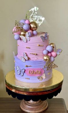 a three tiered cake decorated with butterflies and the name istta on it's side