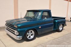 an old blue pickup truck parked in front of a building with no one around it