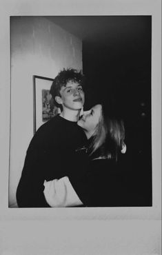 black and white photograph of two people kissing each other in front of a painting on the wall