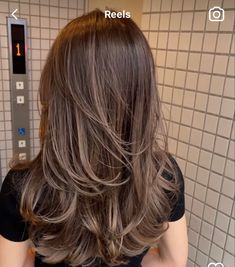 a woman with long brown hair standing in front of a bathroom mirror looking at her reflection