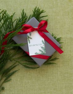 a present wrapped in grey paper with a red ribbon tied around it on a green surface