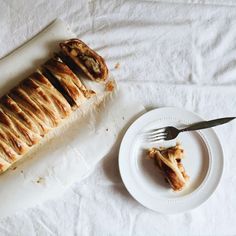 a piece of bread on a plate next to a knife and fork, with another half eaten pastry in the background