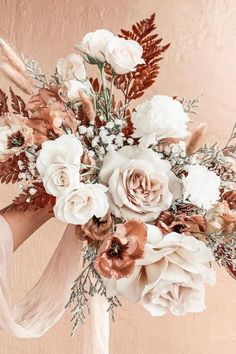 a woman holding a bouquet of flowers in front of a pink wall with white and brown flowers