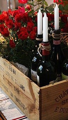 wine bottles and candles in a wooden crate with red roses on the table next to it