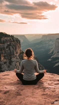 a woman sitting on top of a cliff while meditating