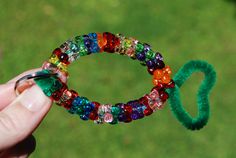 a person is holding a ring made out of beads and green hair tie on the grass