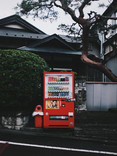 a red vending machine sitting on the side of a road next to a tree