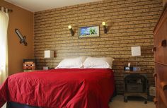 a bedroom with a brick wall and red bedspread on the bed is shown