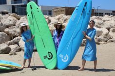 two women standing on the beach with surfboards in front of some rocks and boulders