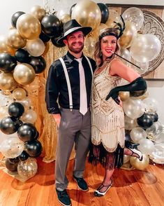 a man and woman posing for a photo in front of balloon arch with black, white and gold balloons