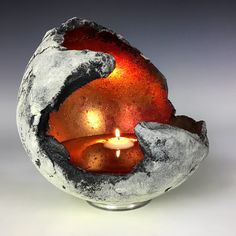 a lit candle in a bowl made out of rock and cement with an orange light inside