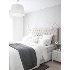 a bed with white linens and pillows in a bedroom next to a lamp on a table