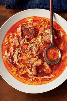 a bowl of meat and tomato soup with a ladle in it on a wooden table