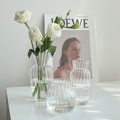 three vases with flowers in them sitting on a white table next to a magazine