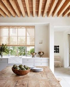 a wooden table topped with plates and bowls filled with fruit next to a kitchen window