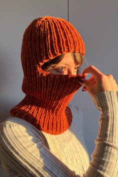 a woman wearing an orange knitted hat and scarf with her hands on her face