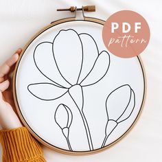 a hand holding a embroidery hoop with a flower drawn on it