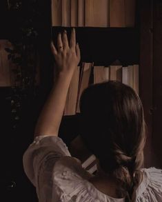 a woman in white shirt leaning against book shelf with her hand on the bookshelf