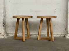 two wooden stools sitting next to each other on concrete floored area with white wall in background