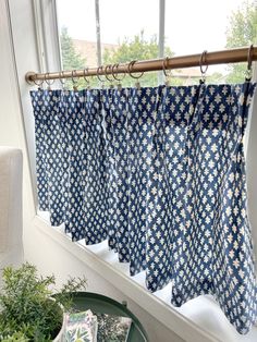 a blue and white curtain hanging in front of a window next to a potted plant