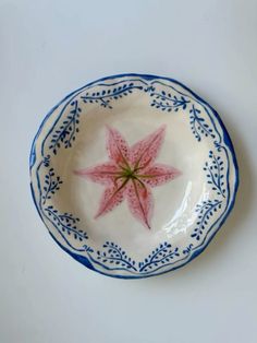 a blue and white bowl with a pink flower on it's rim, sitting on a table