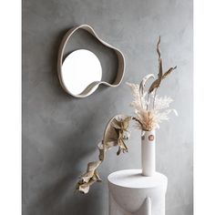 a white vase with flowers in it next to a mirror