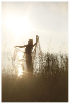 a woman standing in tall grass with her arms spread out and the sun behind her