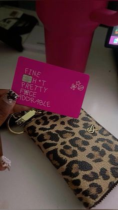 a person holding up a pink card in front of a cell phone and leopard print purse