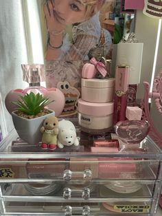 an assortment of cosmetics and other items in a clear case on a table with a poster behind it