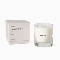 a glass candle next to a box on a white background with the words, warm musk