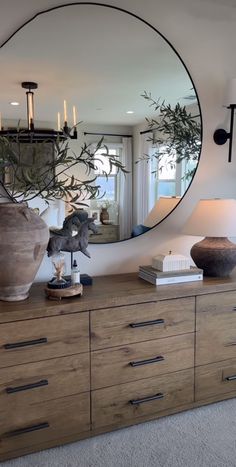 a large mirror sitting on top of a dresser next to a lamp and vases