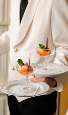 a man in a white suit holding two plates with desserts on top of them