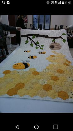 a quilt is being displayed on a table with people in the background looking at it