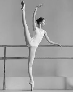 a woman in white leotard and ballet shoes standing on one leg with her arms stretched out