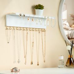 a white shelf with many necklaces hanging from it's sides next to a mirror