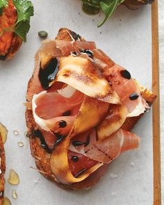 an open faced sandwich with meat and vegetables on it sitting on a cutting board next to other food items