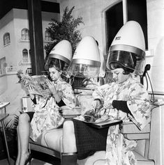 two women sitting in chairs with helmets on their heads and one reading a magazine while the other is eating