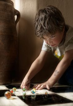 a young boy is playing with marbles on the floor in front of a vase