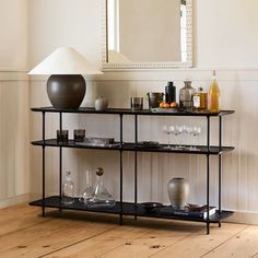 a shelf with wine glasses and bottles on it in front of a wall mounted mirror