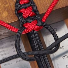 a red and black rope is tied to a piece of wood with measuring tape in the background