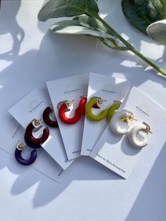 five pairs of earrings sitting on top of a white table next to a green plant